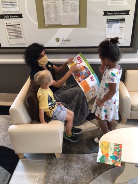 Person in mask reading a book to a child and a teen