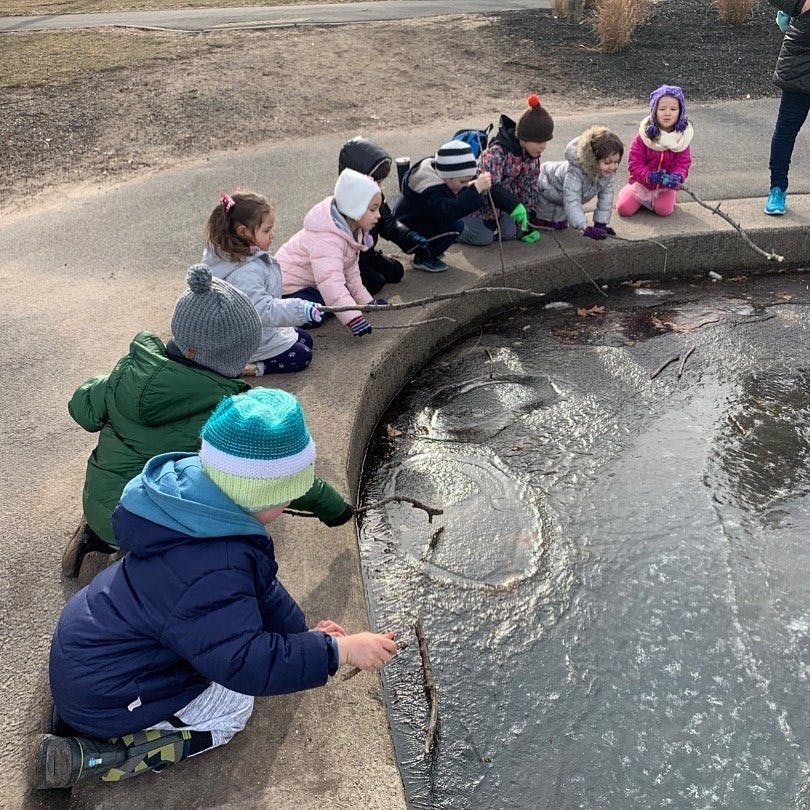 Children kneeling by a frozen puddle, poking at the ice with sticks