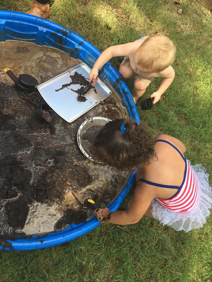 Two children playing in a muddy blue kiddie pool