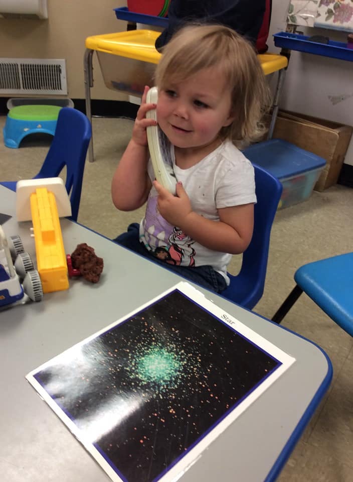 Child holding a toy phone to their ear at a table