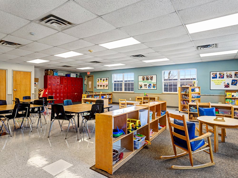 Classroom with tables, chairs, storage shelves, and red lockers