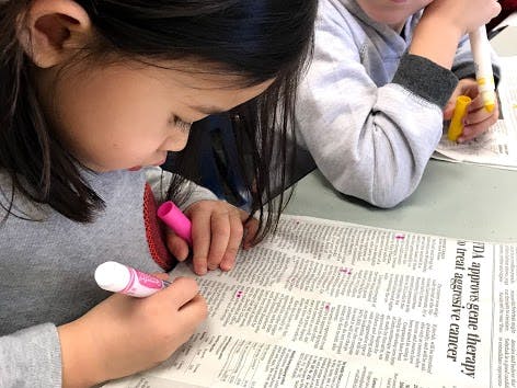 Child marking text on a newspaper with a pink marker