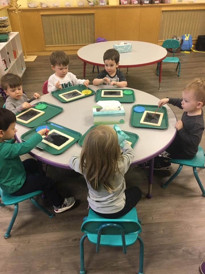 Children sitting around a table with activity trays in a classroom