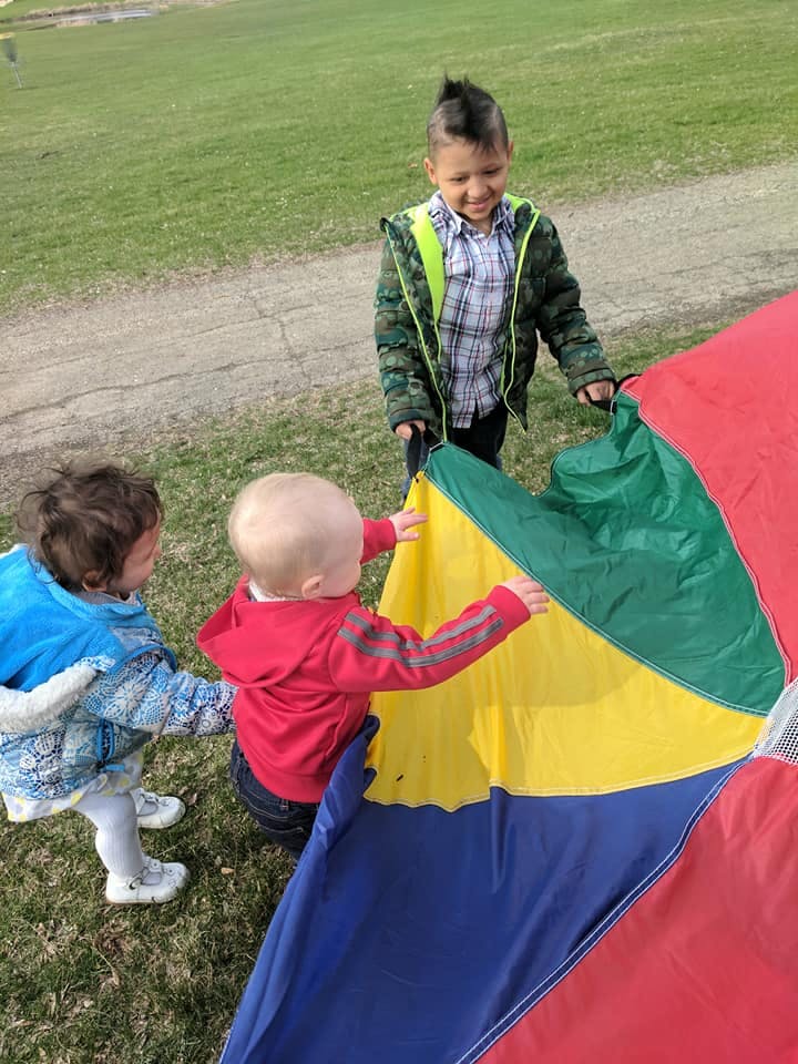 Three children playing with a colorful parachute on a grassy area
