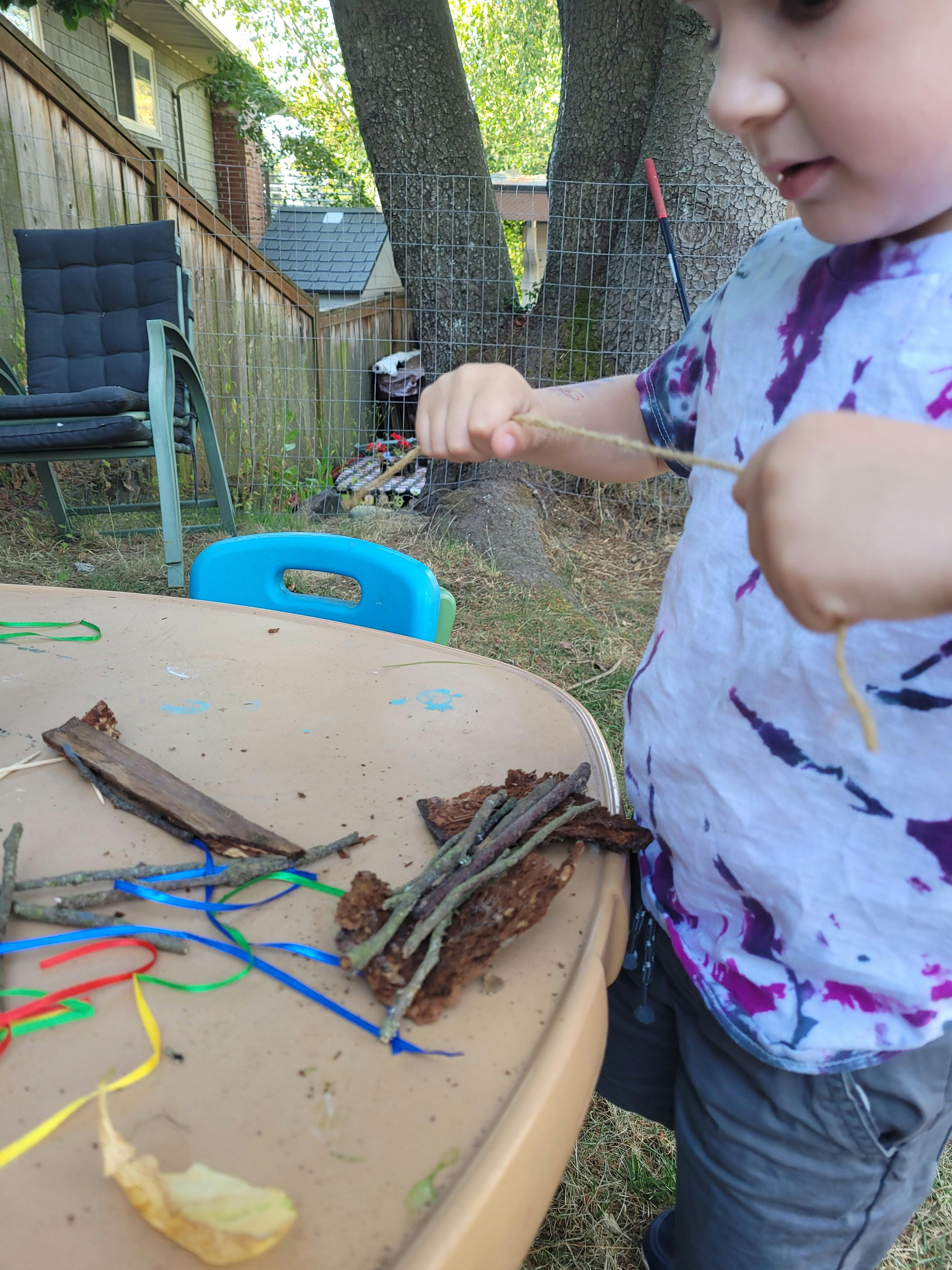 Child playing with sticks and ribbons on a table outdoors