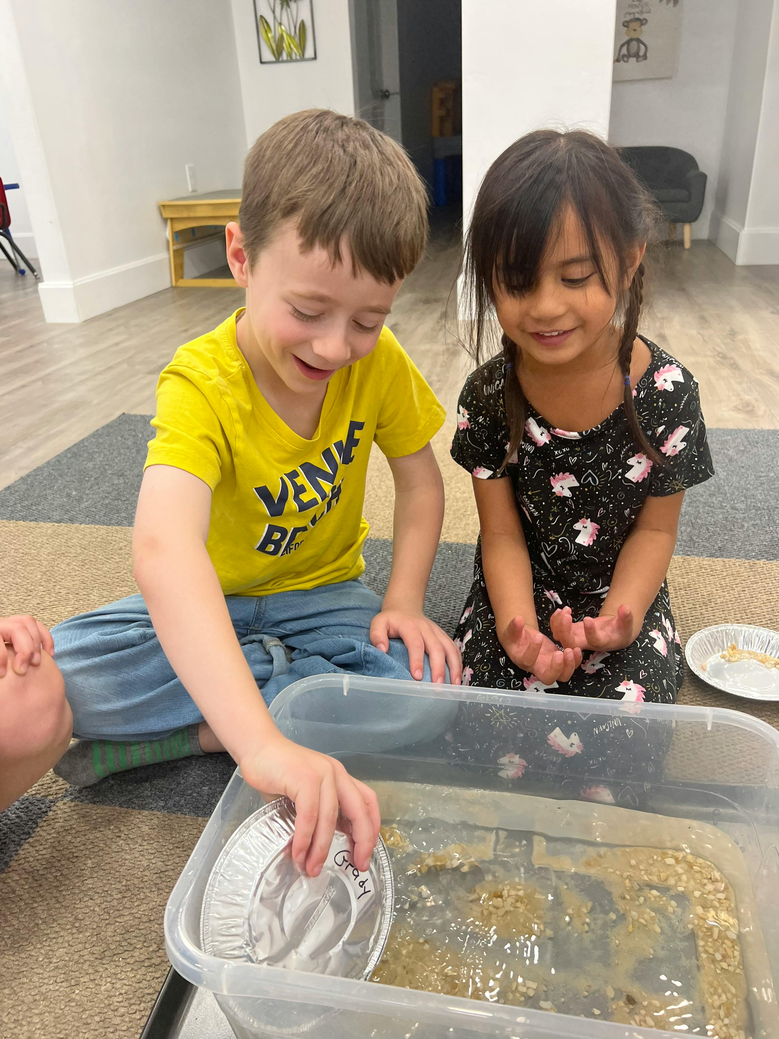 Two children playing with a container of water and small objects