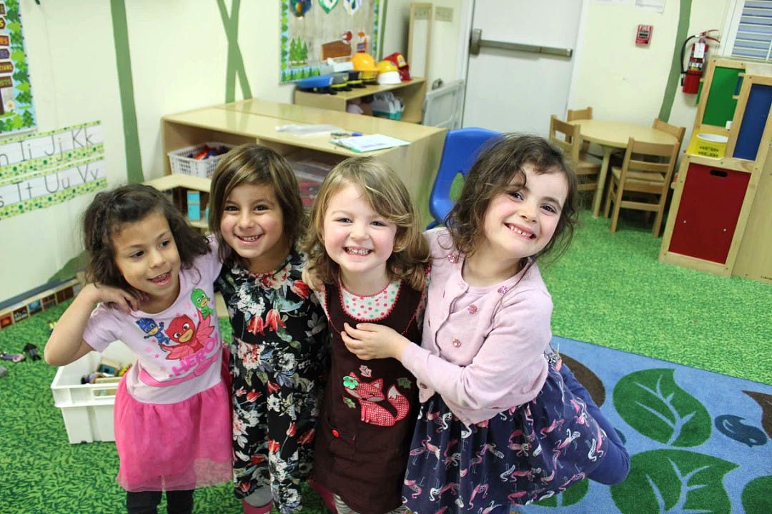 Four children smiling and standing together in a classroom