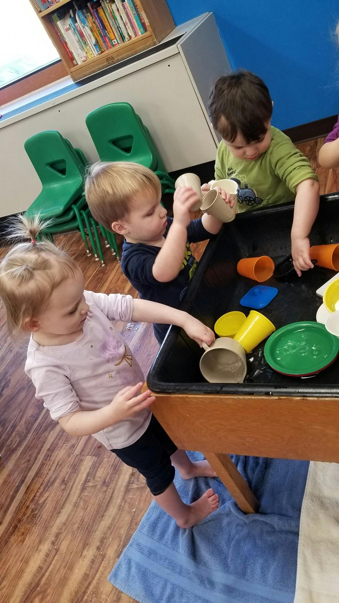 Three children playing with cups and containers in a water table