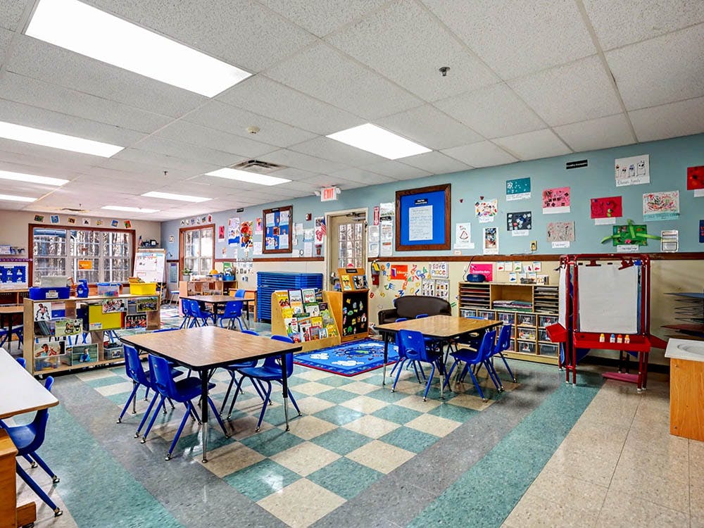 Empty classroom with small tables and chairs, artwork on walls, and learning materials
