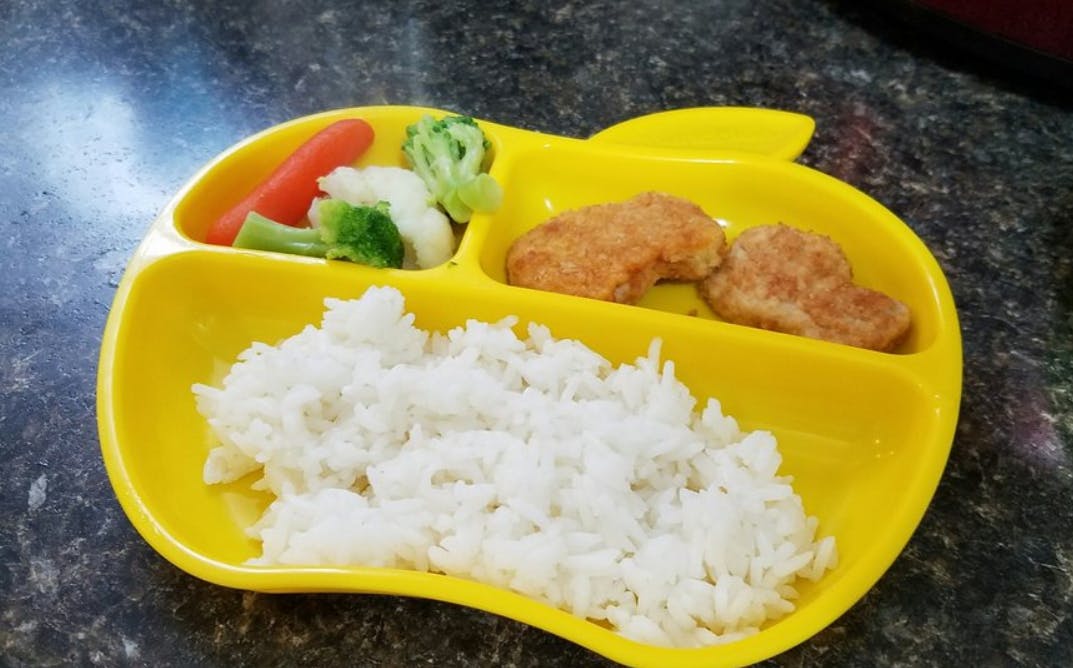 Yellow divided plate with rice, chicken nuggets, and vegetables