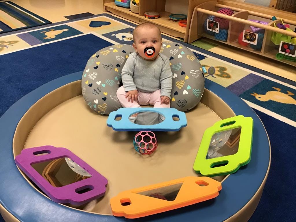 Child with pacifier sitting in a play area with toys