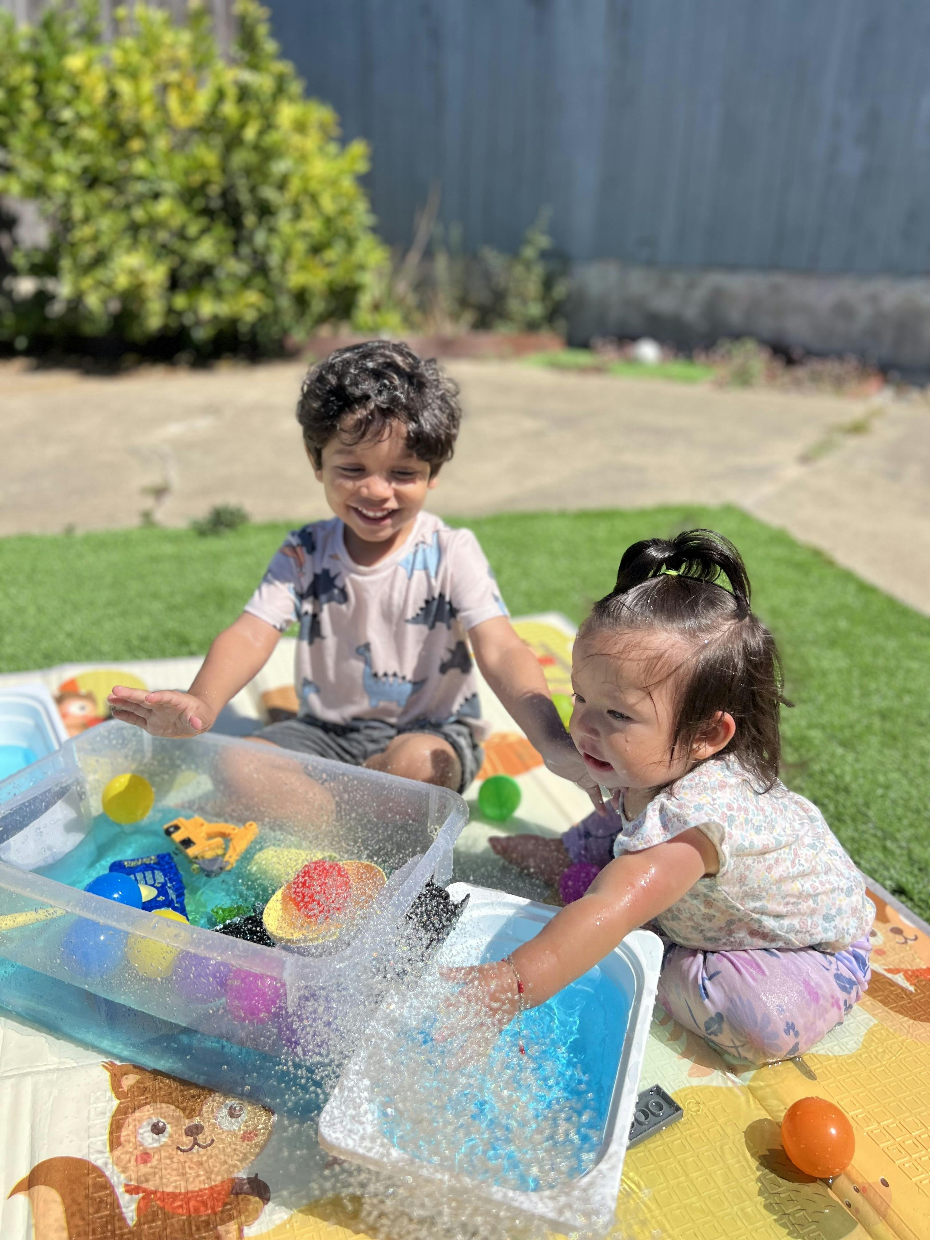 Two children playing with water and toys in plastic bins outdoors