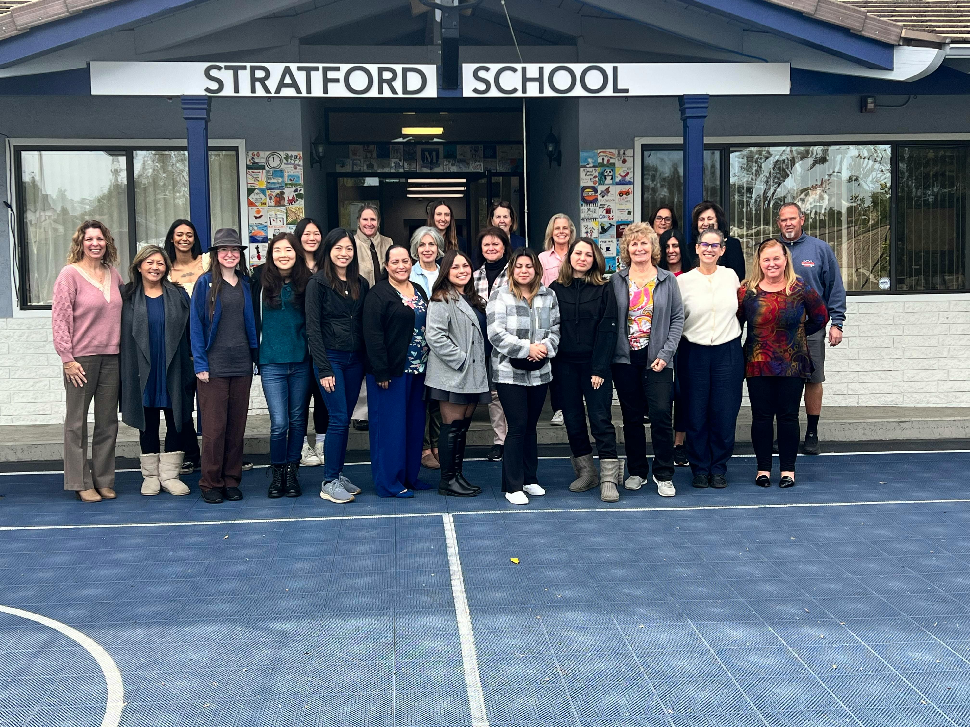 Group of adults standing in front of a building with "STRATFORD SCHOOL" on it