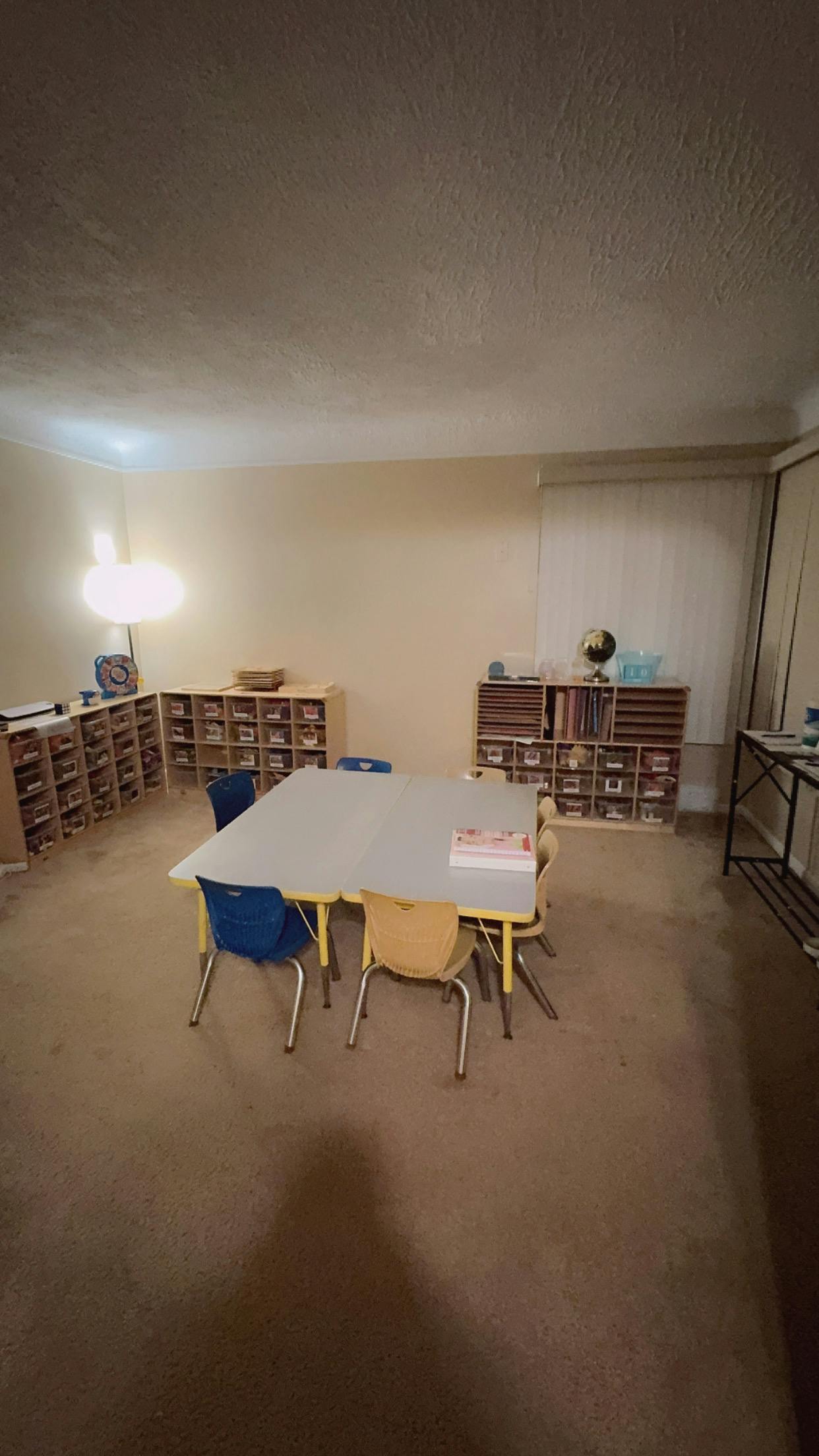 Classroom with small tables and chairs, storage shelves along walls