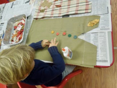 Child gluing colorful buttons onto green fabric