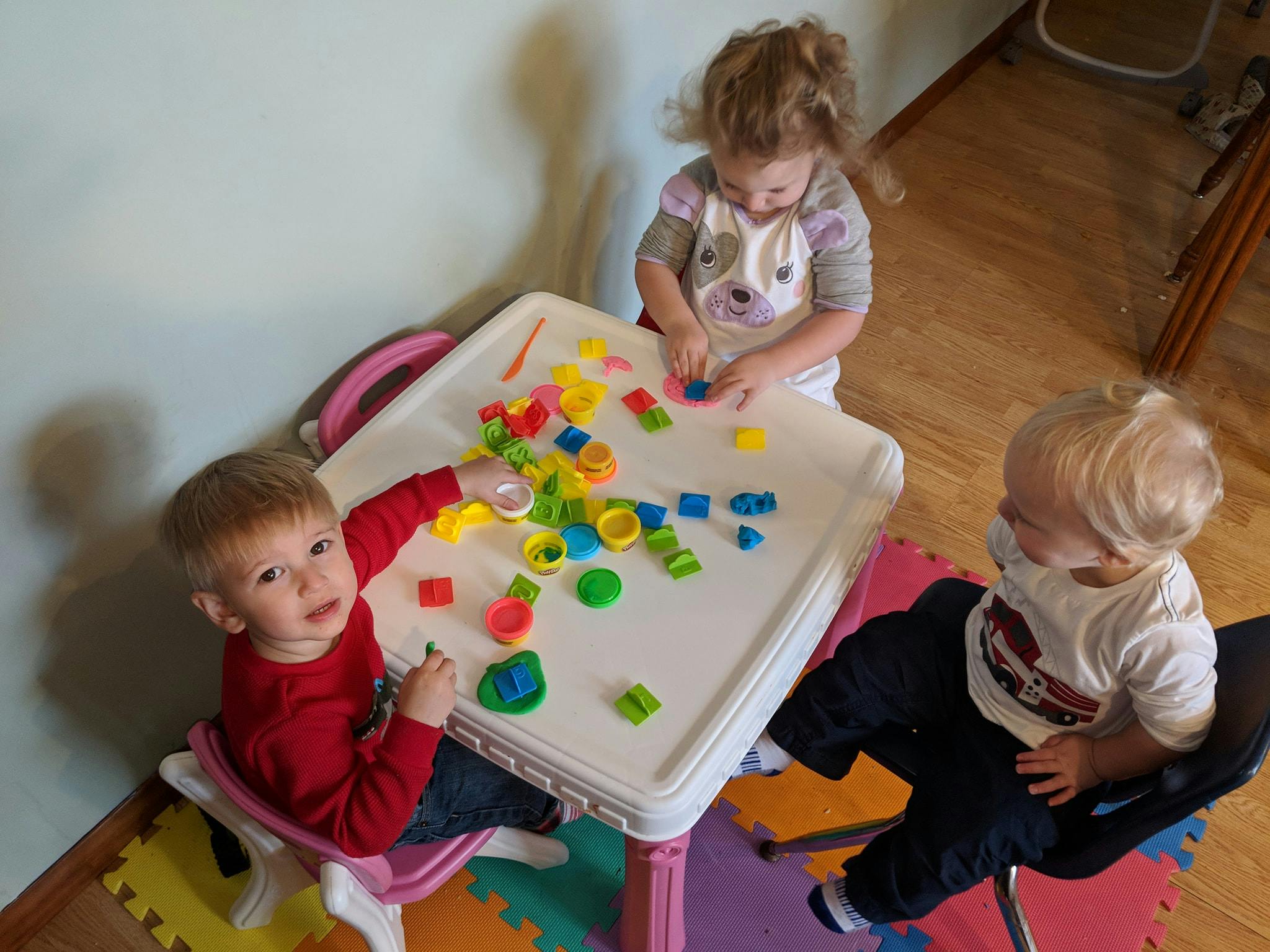Three children playing with colorful toys at a table