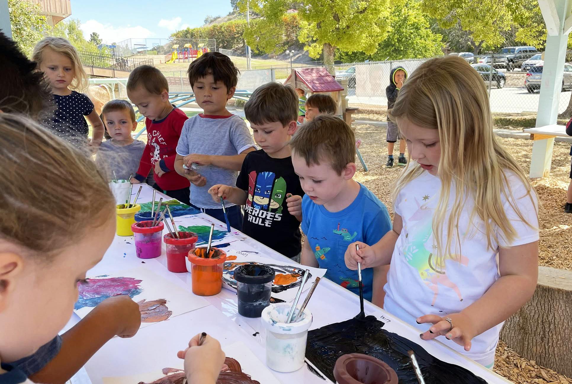 Group of children painting at a table outdoors