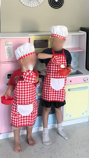 Two children in chef hats and aprons playing in a toy kitchen