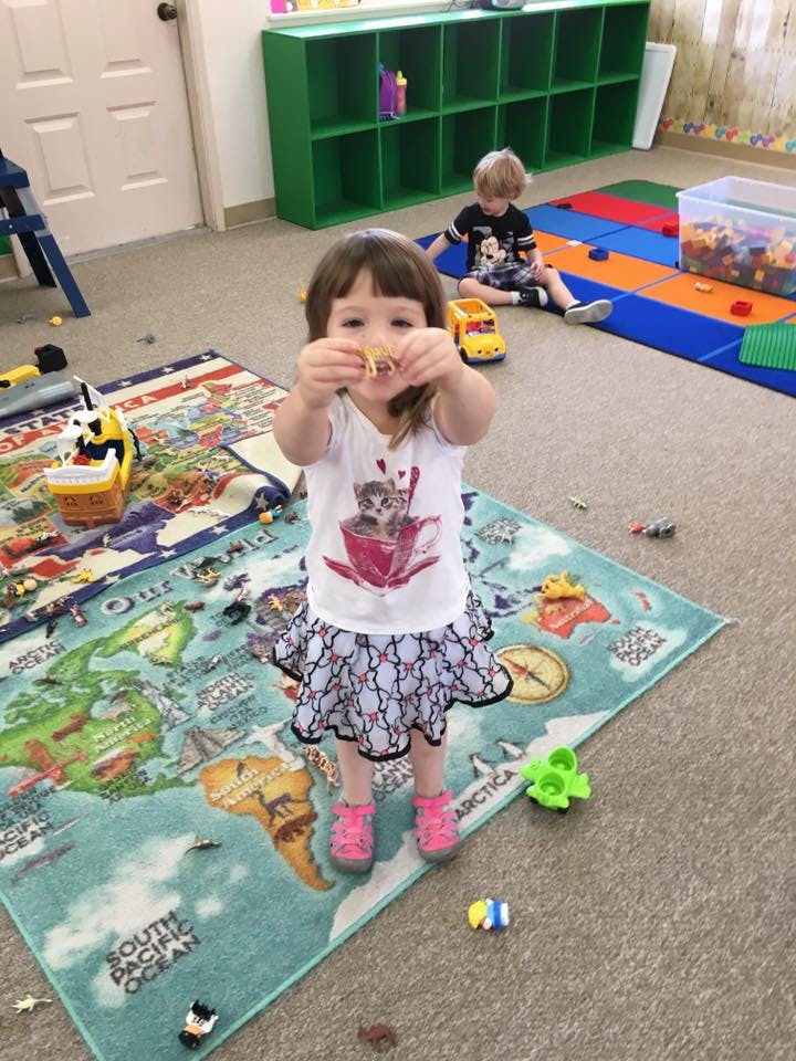 Child standing on a world map rug, holding up a small toy