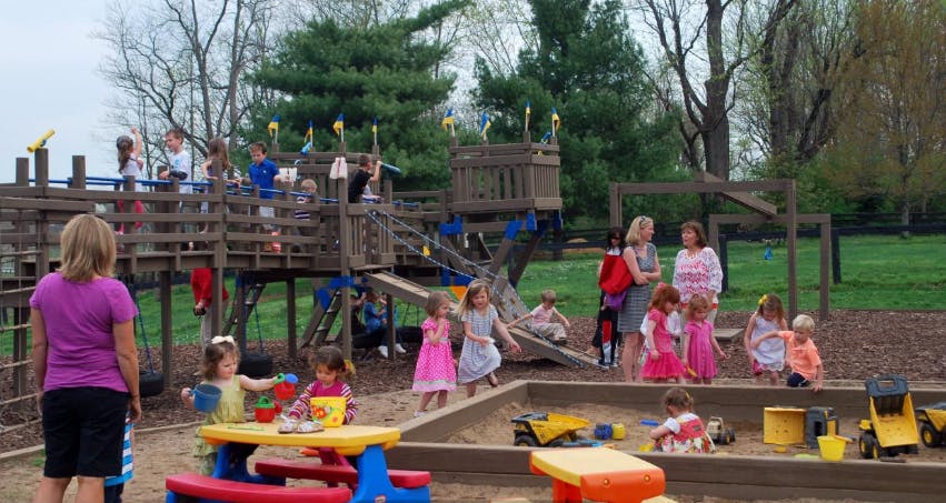 People and children playing on a wooden playground structure and in a sandbox
