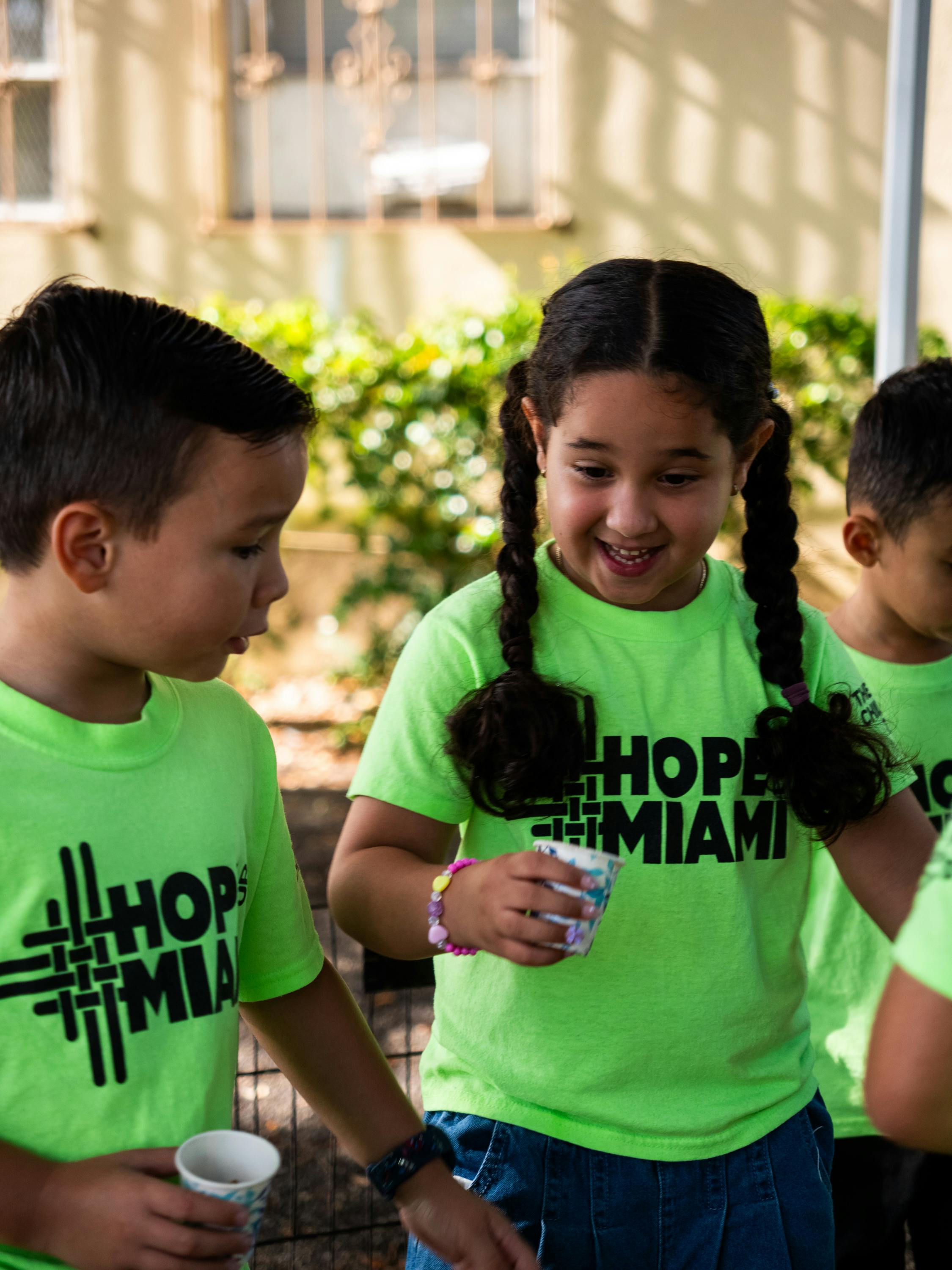 Children in neon green shirts with Hope Miami logo holding small paper cups