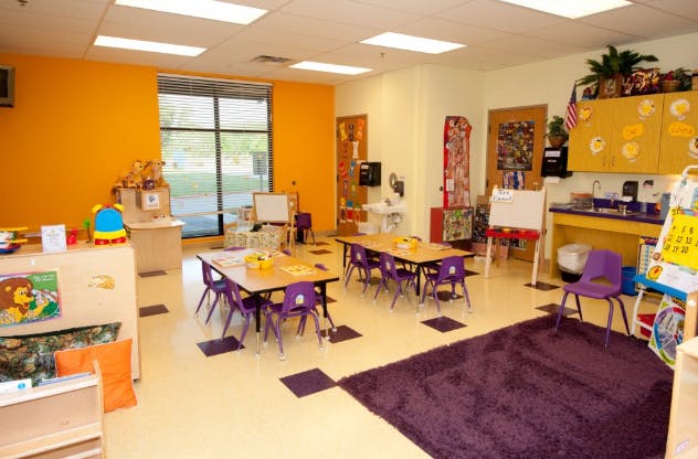 Classroom with small tables and chairs, a purple rug, and a large window