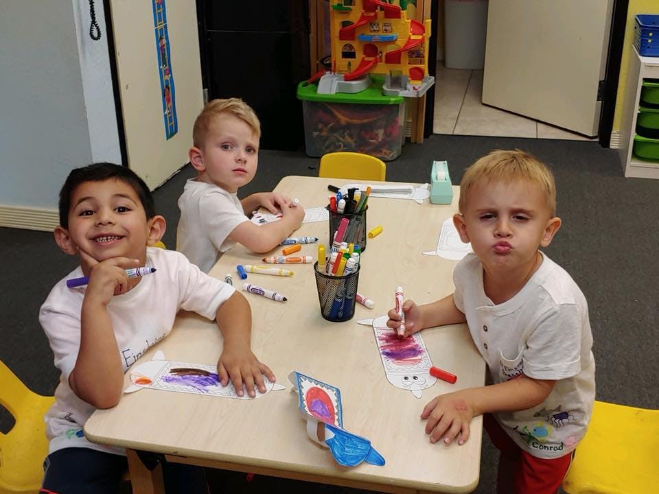 Three children sitting at a table with markers and paper