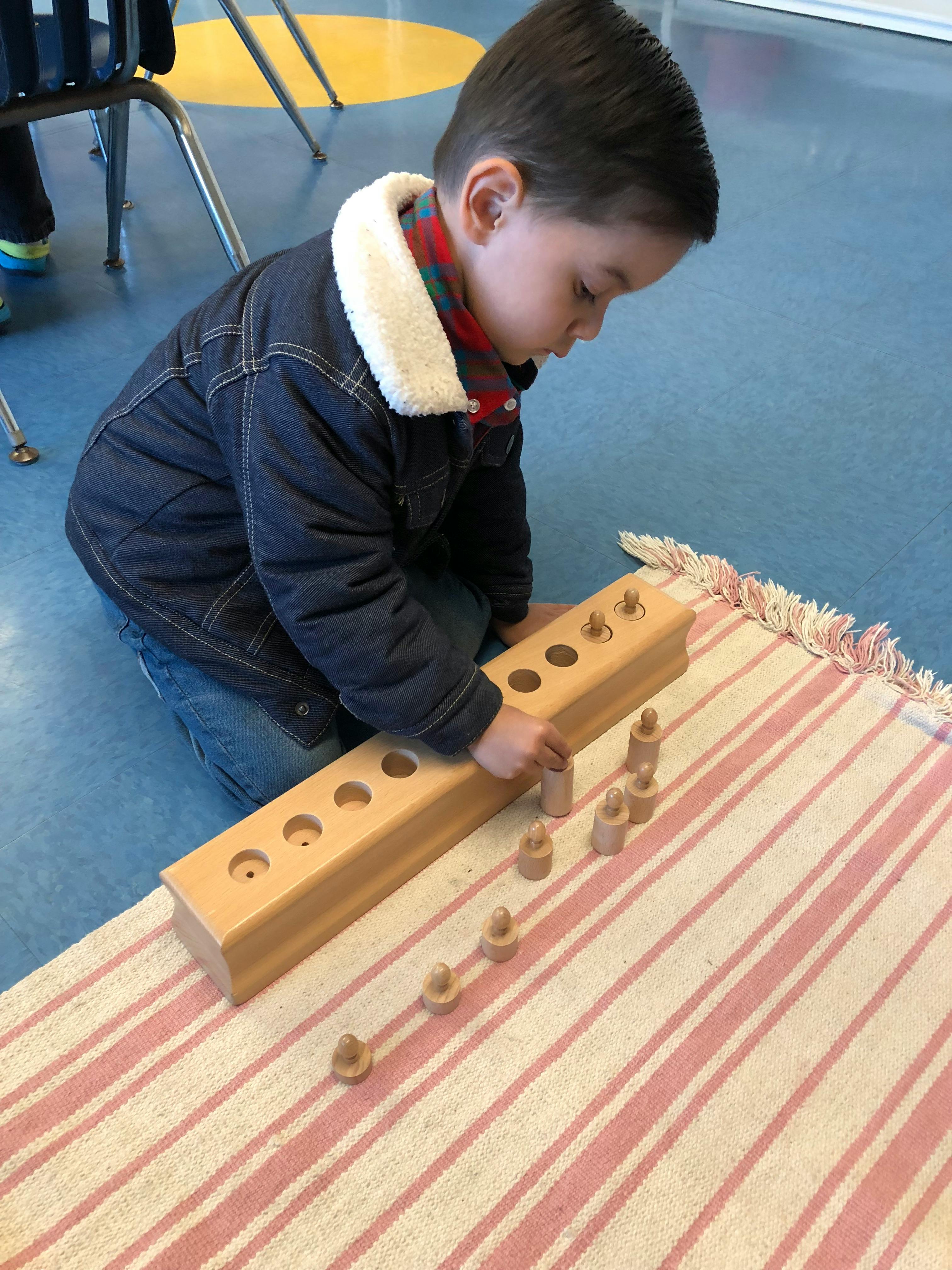 Child kneeling on a rug, placing wooden pegs into a wooden block