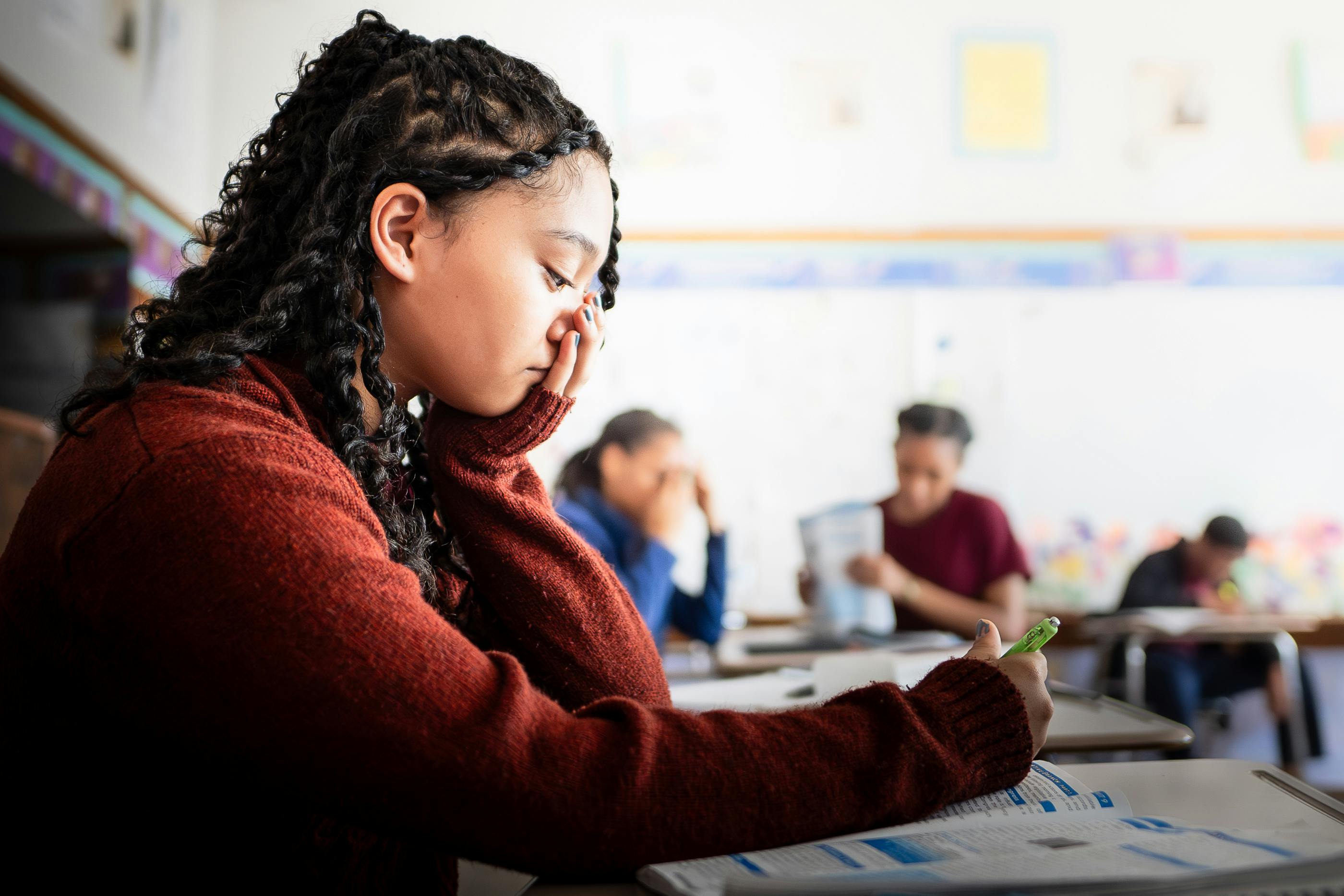 Teen in a classroom resting head on hand while looking at papers