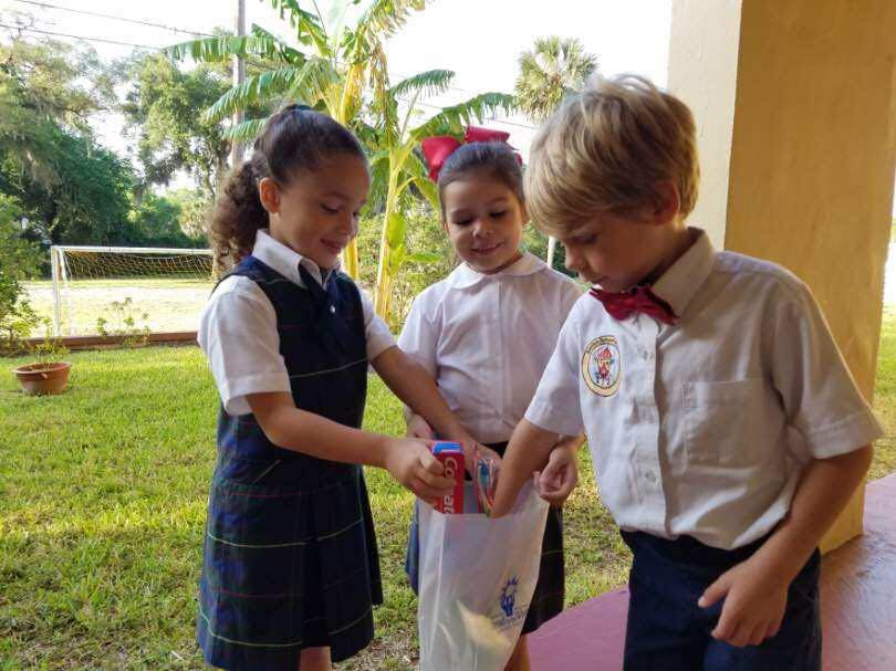 Three children in school uniforms holding a small object together