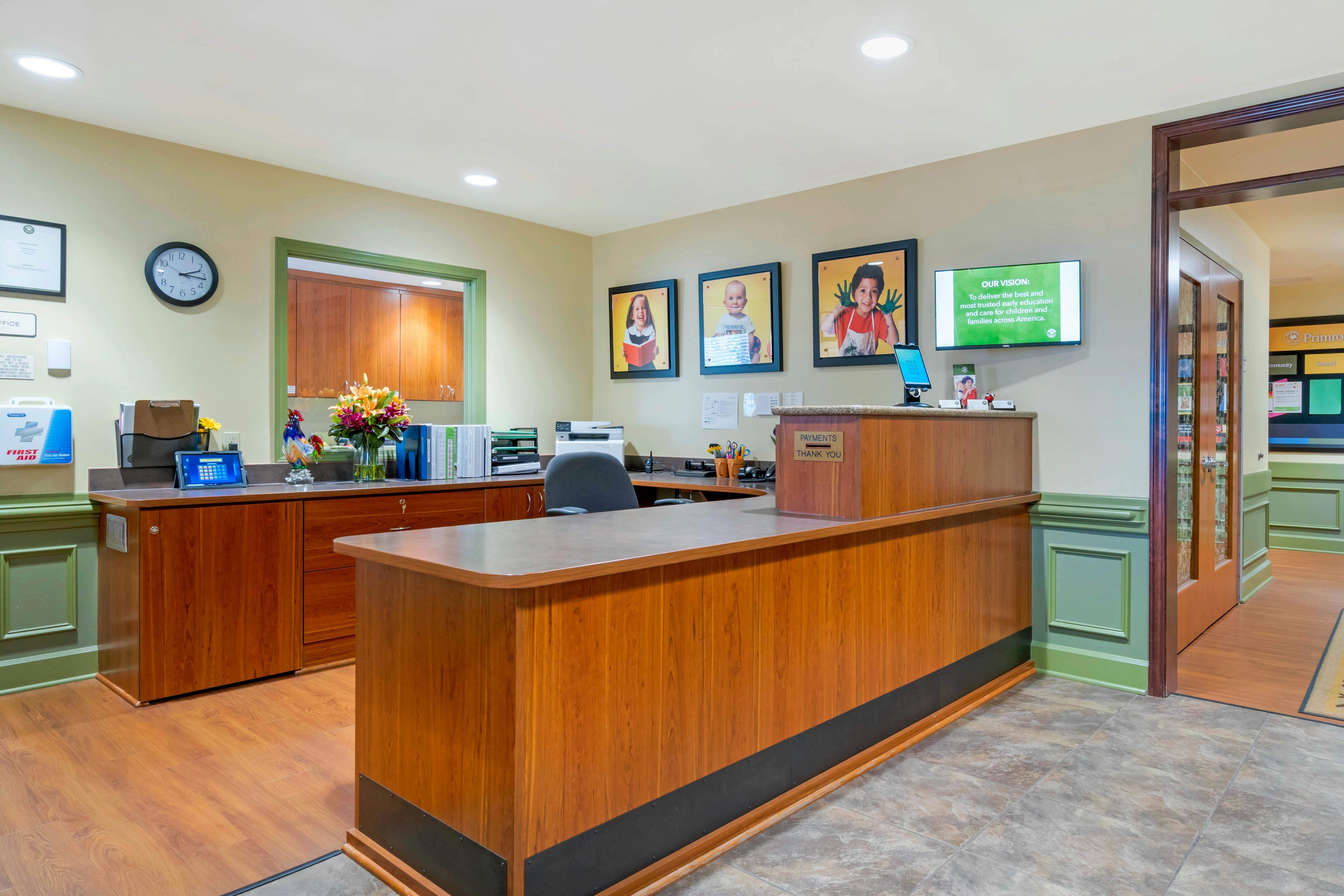 Reception desk with “Payments Thank You” sign, photos of children, and a screen with "Our Vision" text