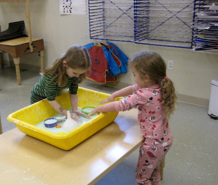 Two children playing with water in a yellow bin