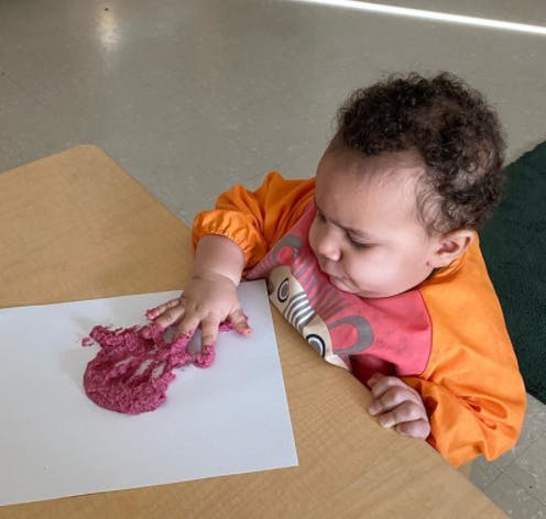 Child playing with pink paint on paper