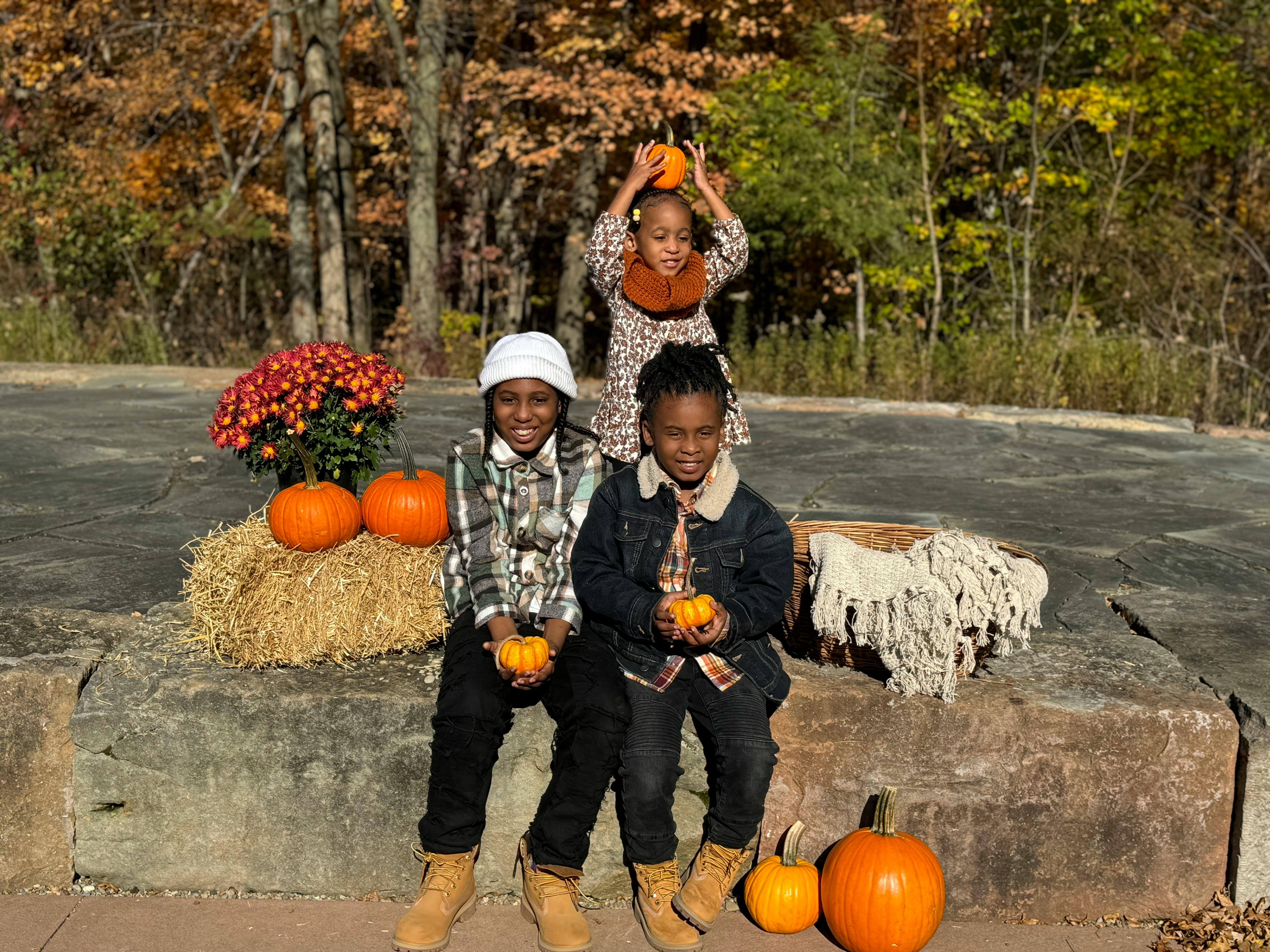 Three children with pumpkins, two sitting and one standing behind them