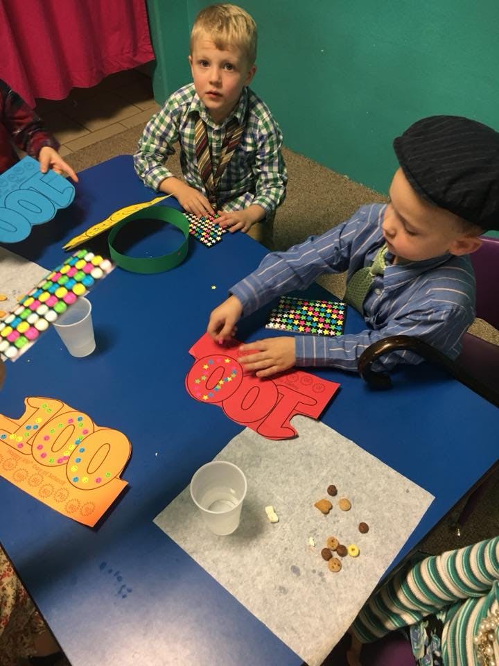 Two children at a table doing a craft activity with "100" cutouts