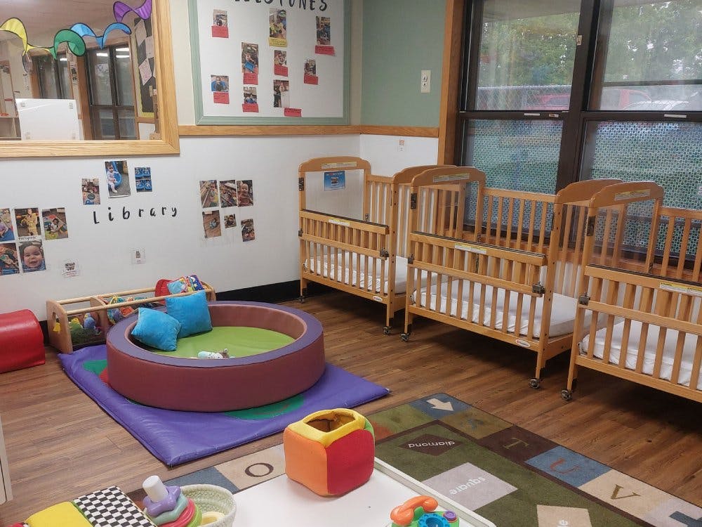 cribs in a classroom with a play area and alphabet rug