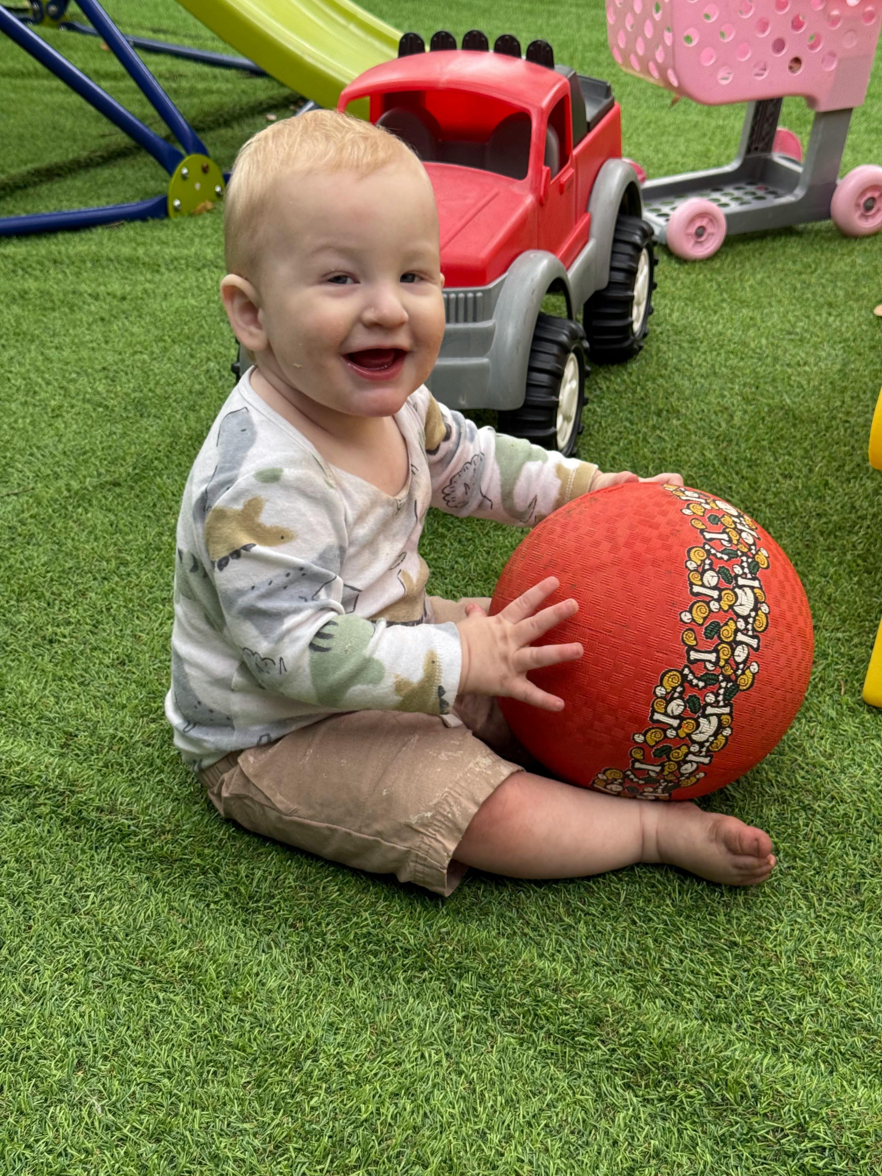 Child sitting on artificial grass playing with a ball