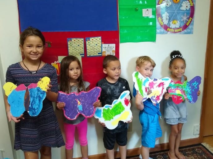 Five children holding up colorful butterfly crafts