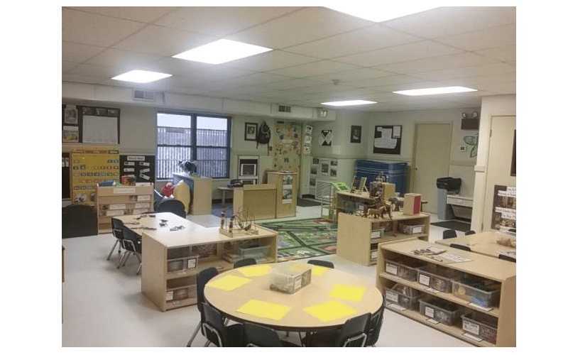 Classroom with small tables and chairs, shelves with toys, and a rug on the floor