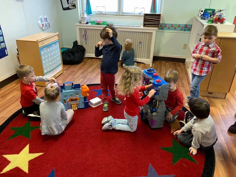 Children playing with toys on a red rug in a classroom