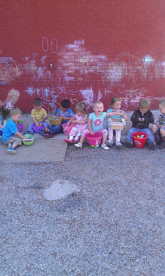 Children sitting with baskets and buckets along a red brick wall