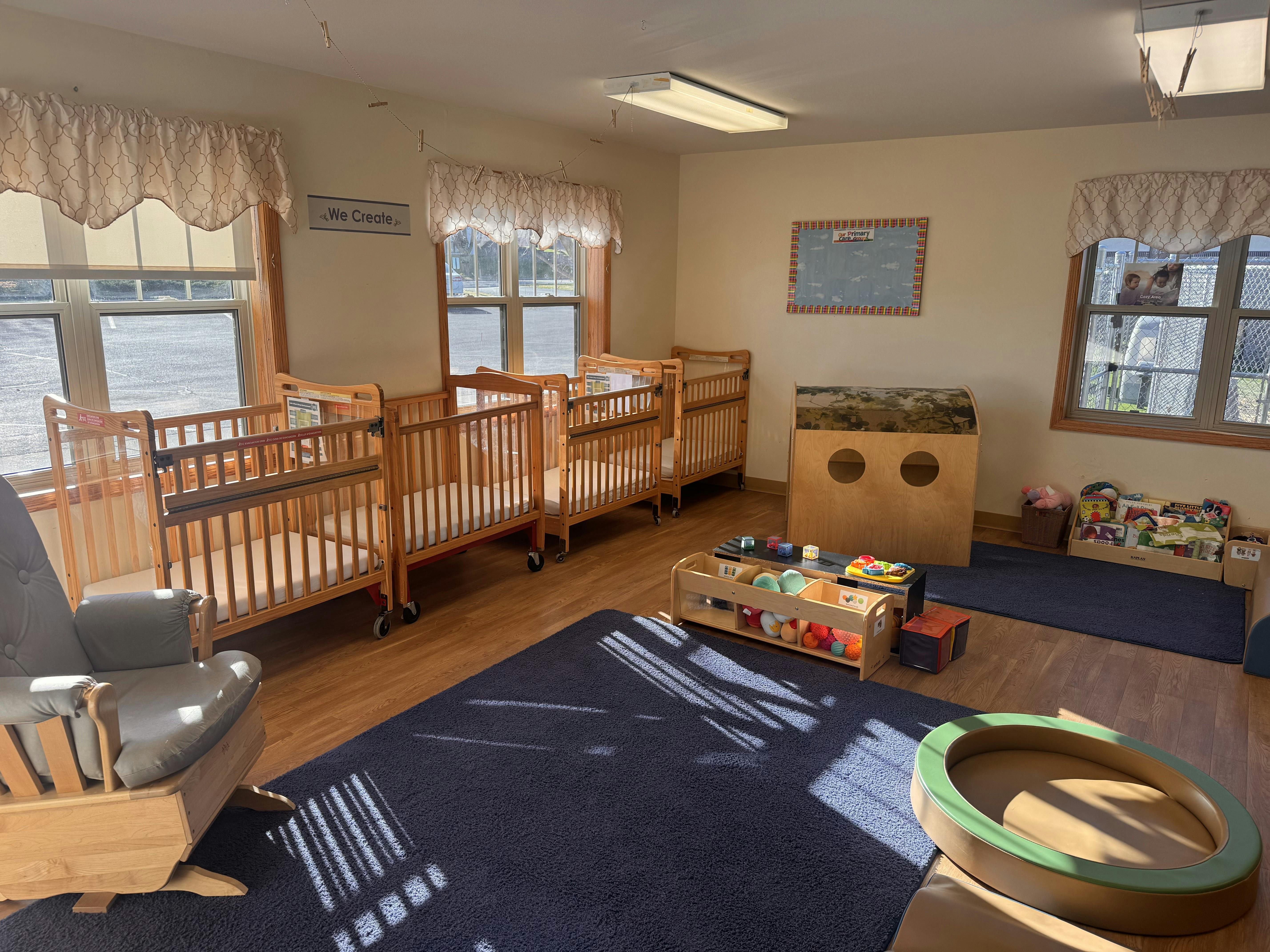 Baby room with several cribs, a rocking chair, and play items on rugs