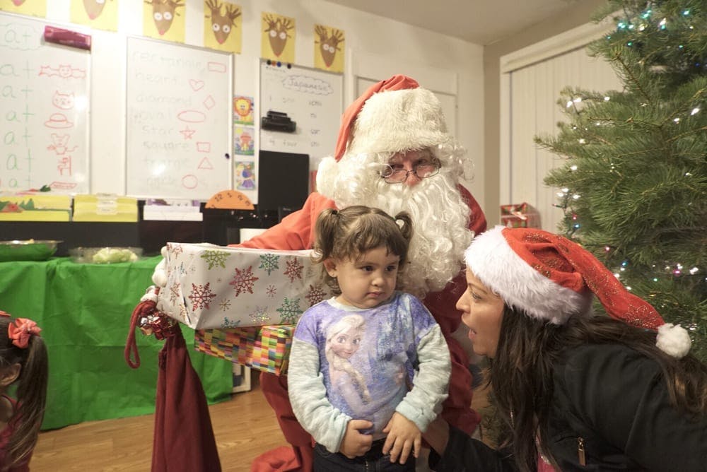 Person dressed as Santa Claus with a child and another person in a Santa hat