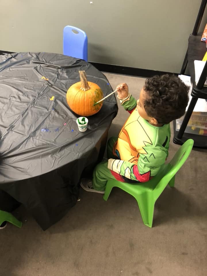 Child painting a pumpkin at a table