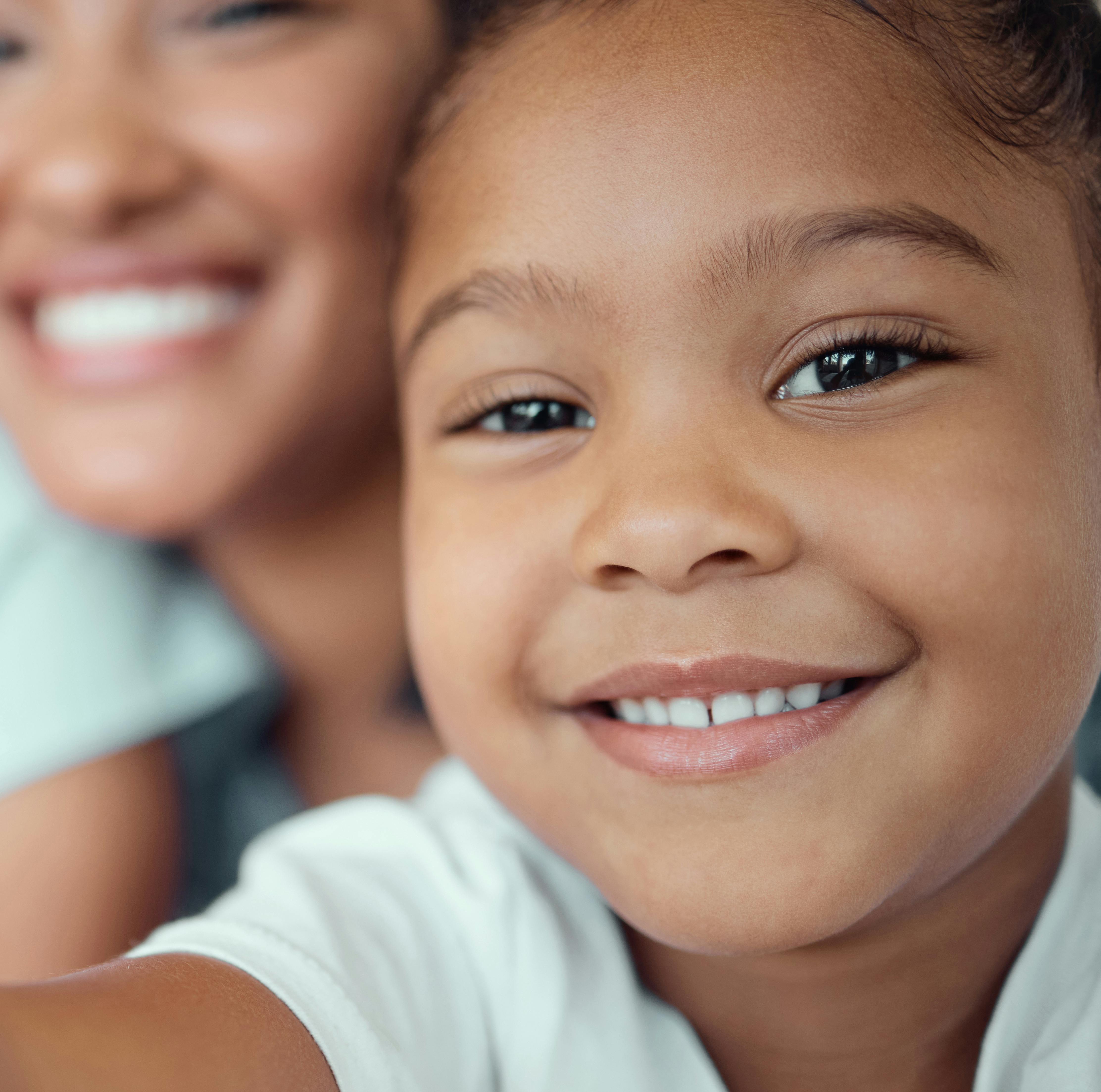 Smiling child in a white shirt and blurry adult behind them