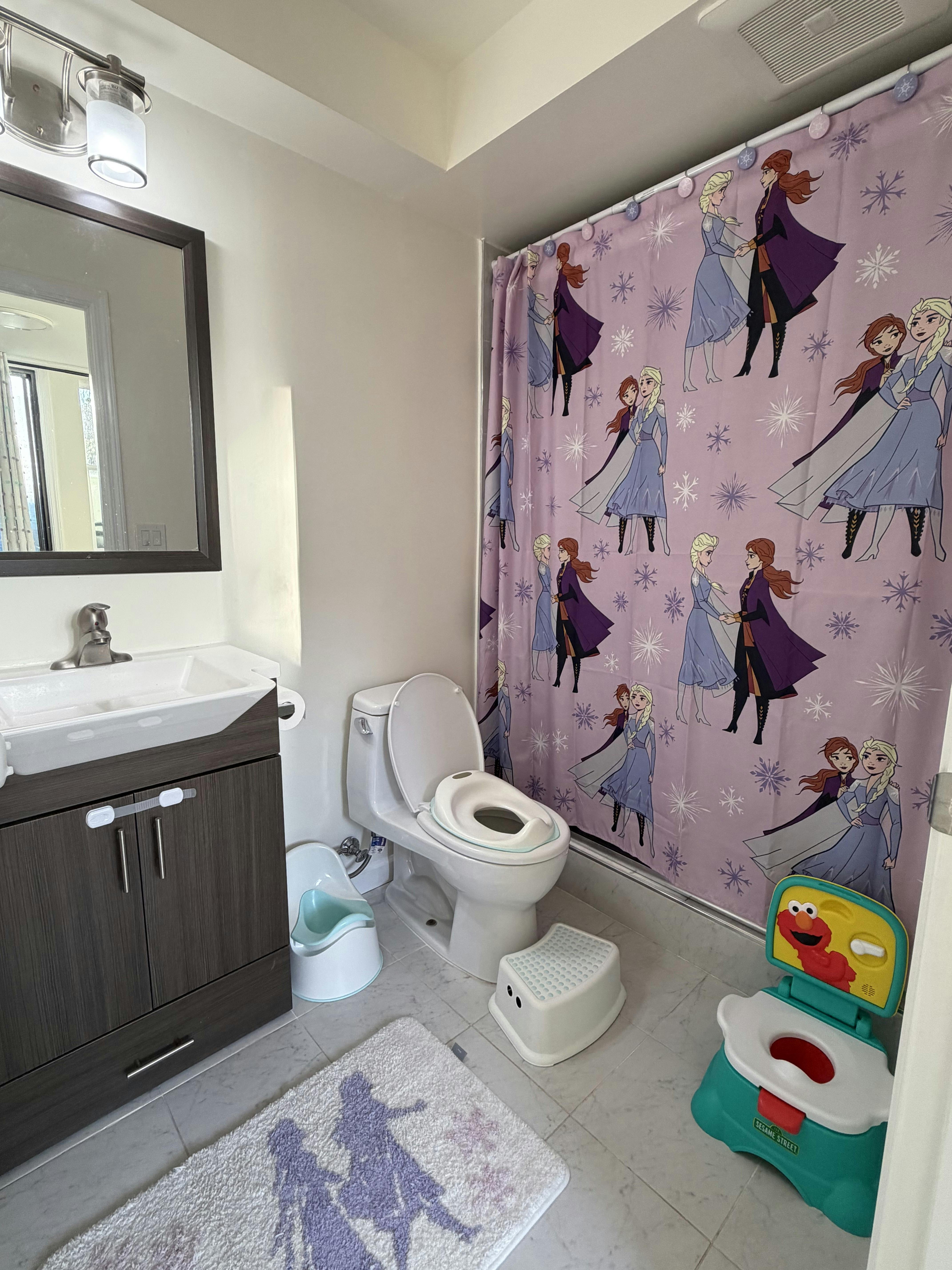 Bathroom with child-sized potty seats and a character-themed shower curtain