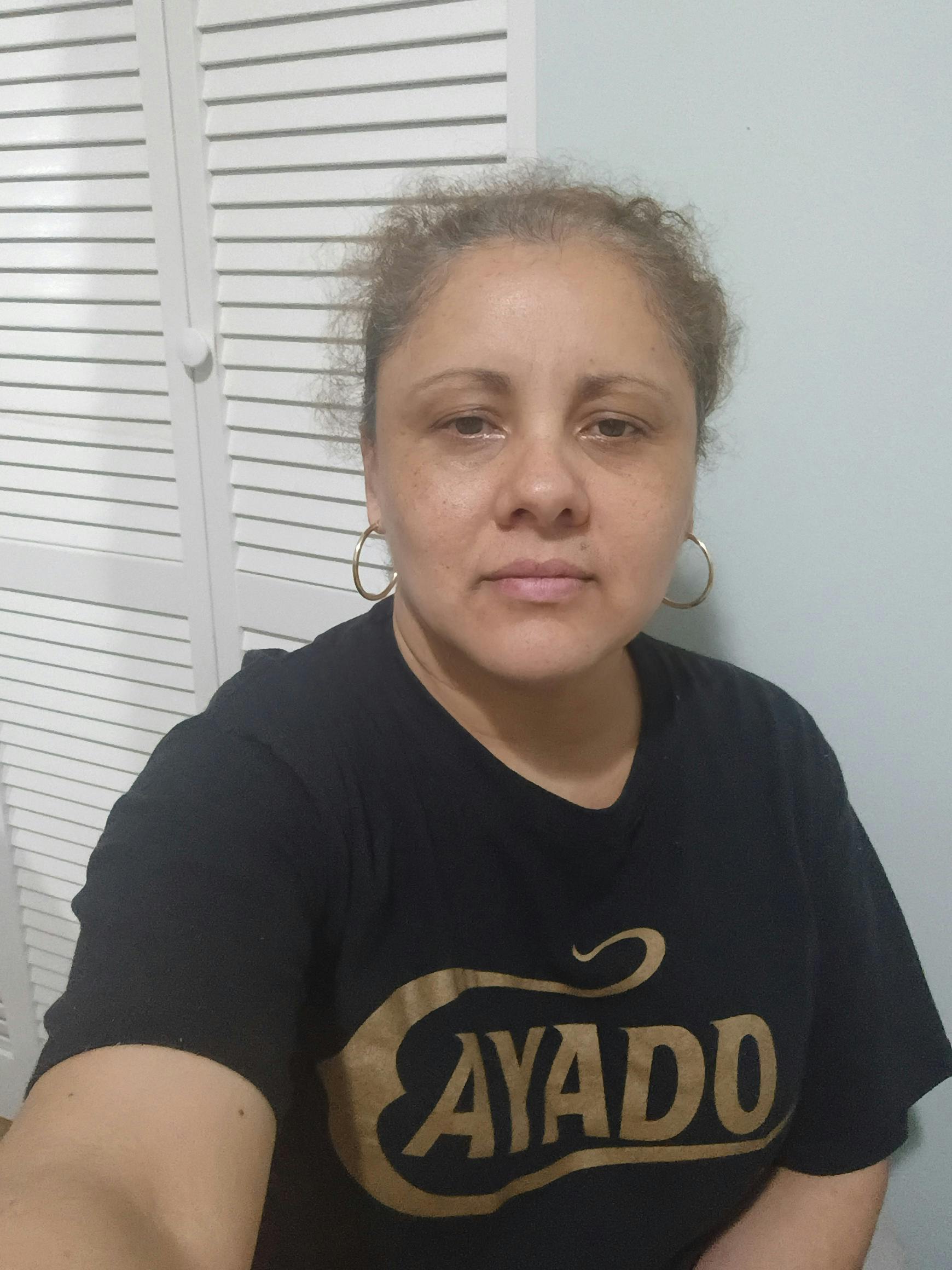 A person wearing a black t-shirt with gold text in front of a louvered door