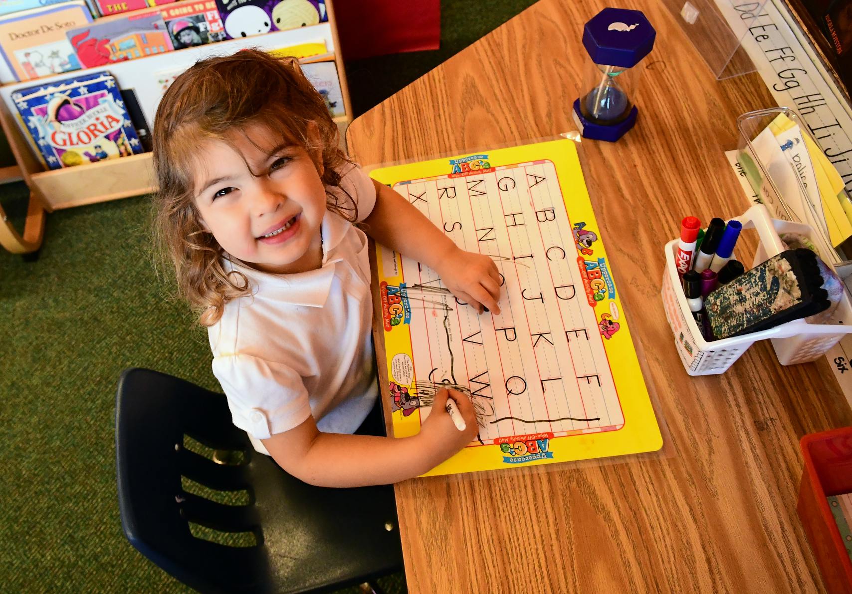 Child writing on an alphabet tracing board at a table