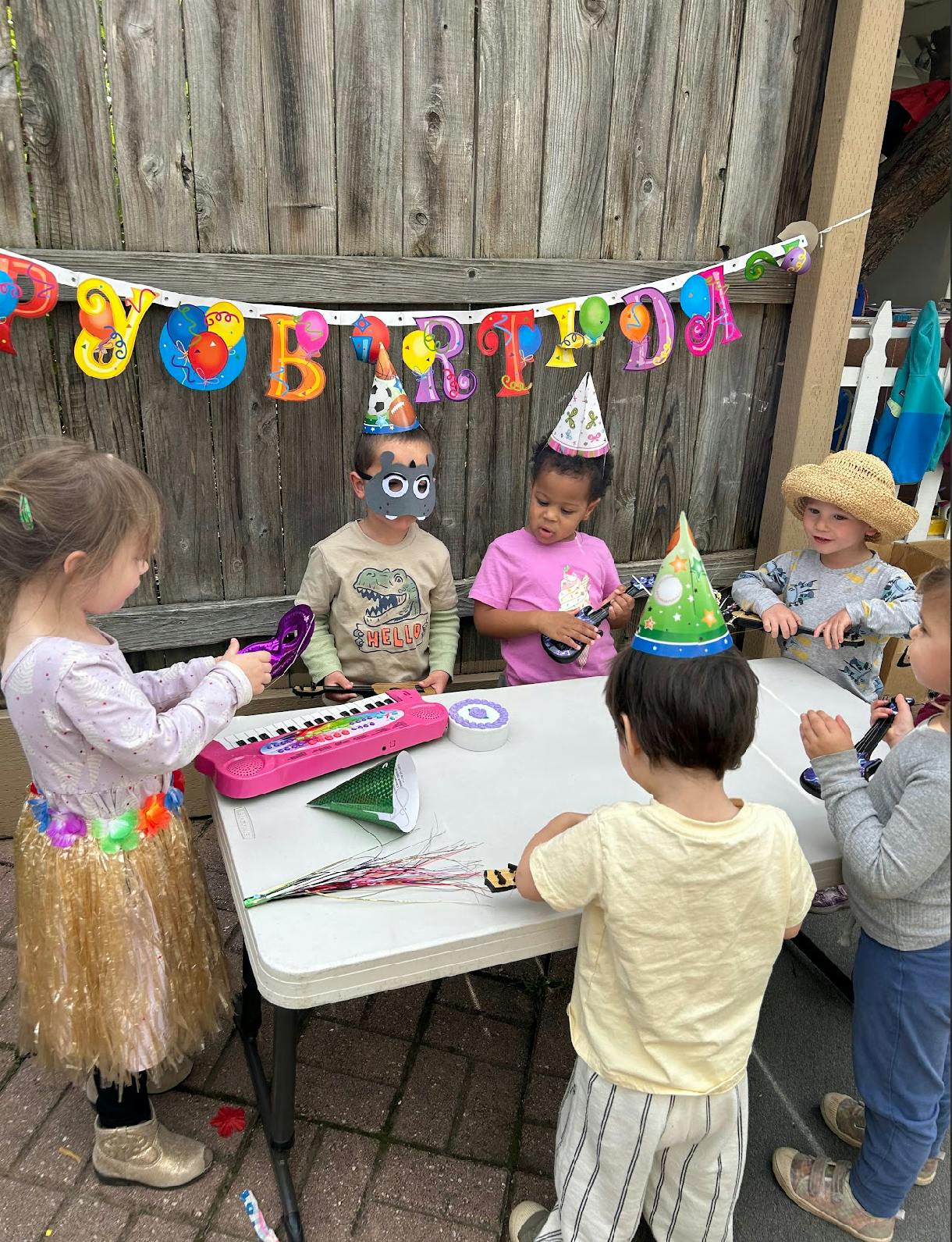 Children in party hats gathered around a table with a "Happy Birthday" banner
