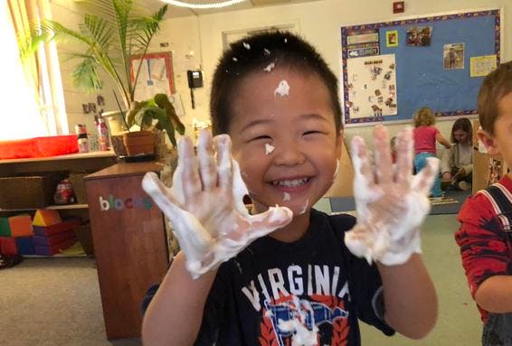 Child with foam on hands and face in a classroom